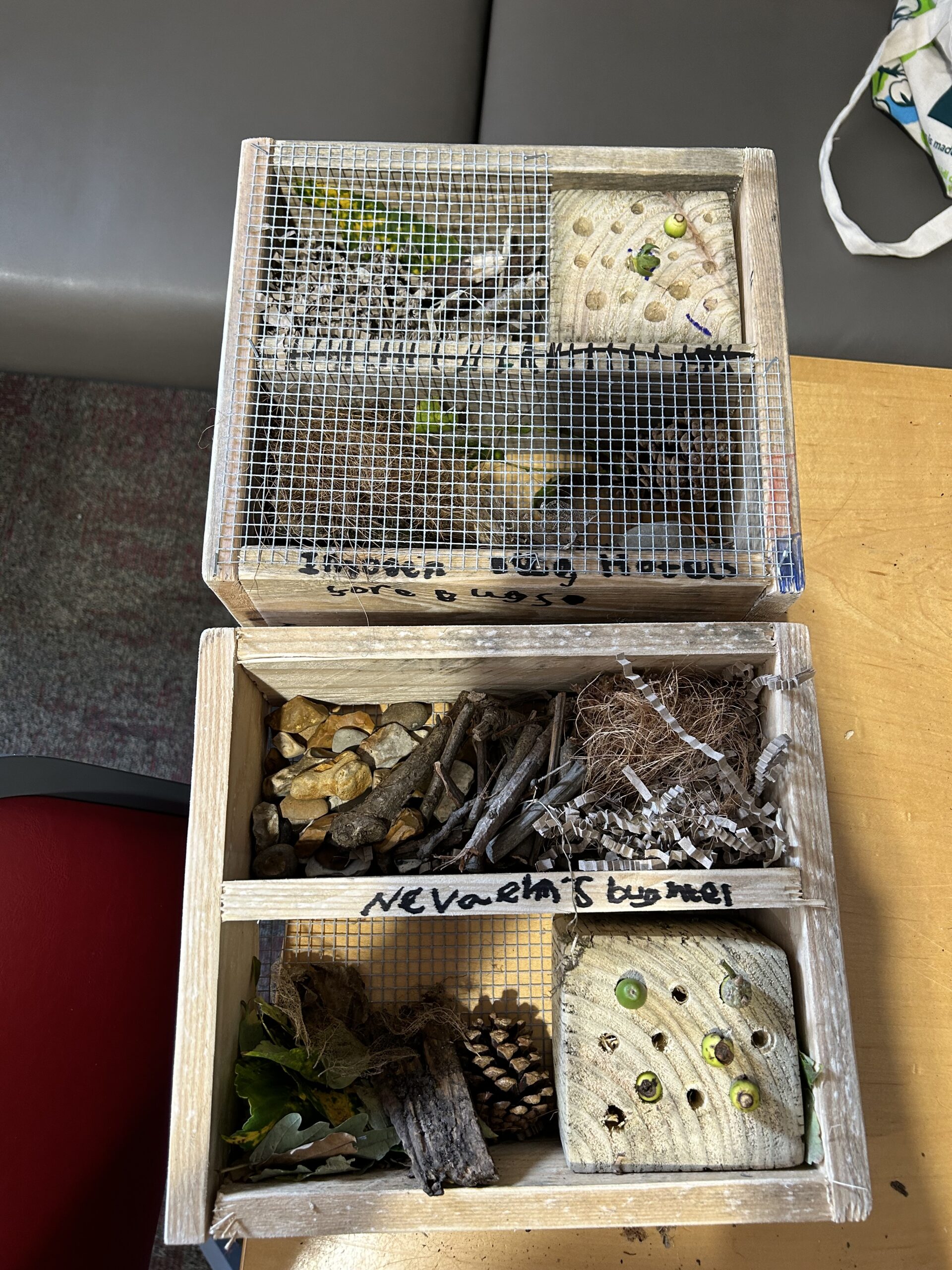 A bug hotel made from various natural materials such as wooden logs, twigs, pine cones, and dried leaves. The structure is divided into multiple compartments, each filled with different materials to attract a variety of insects. The bug hotel is placed in a garden setting, surrounded by greenery and flowers, providing a safe habitat for insects like bees, ladybirds, and beetles.