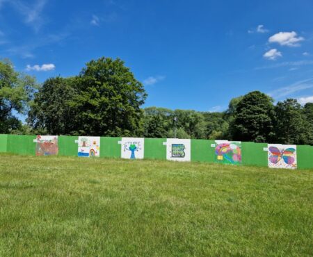 Colourful hoarding artwork displayed at the Brighouse Flood Alleviation Scheme site, created collaboratively by local charities and young people. The artwork features vibrant illustrations, messages of community resilience, and environmental themes, bringing creativity and awareness to the flood protection project.