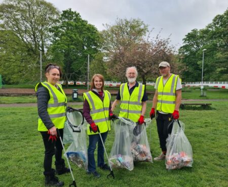 A group of volunteers litter picking at Wellholme Park, Brighouse. All four volunteers are wearing high vis jackets and holding bin bags and litter picks.