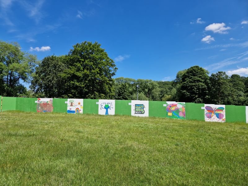 Colourful hoarding artwork displayed at the Brighouse Flood Alleviation Scheme site, created collaboratively by local charities and young people. The artwork features vibrant illustrations, messages of community resilience, and environmental themes, bringing creativity and awareness to the flood protection project.